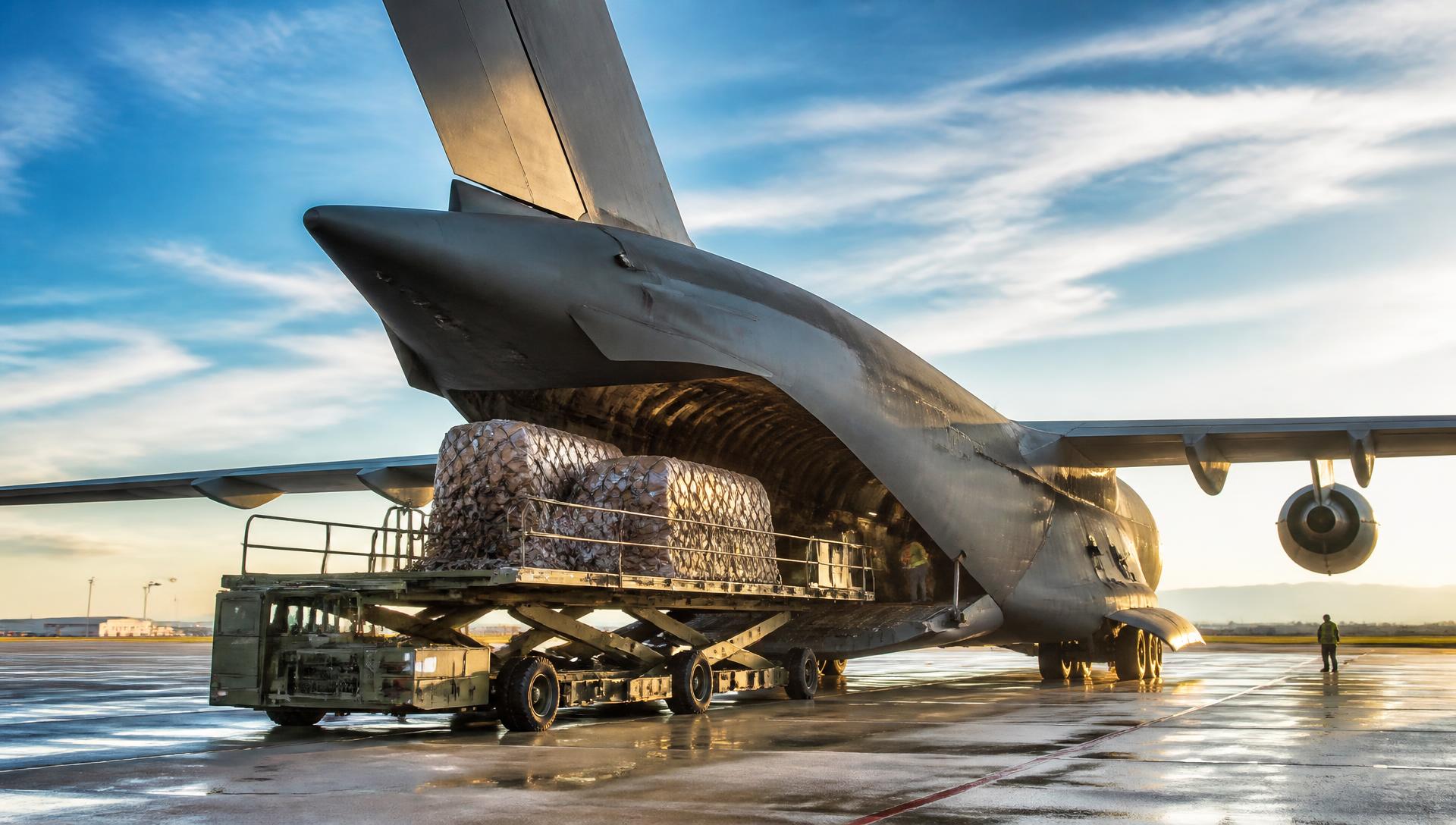 Military cargo aircraft loading palletized freight on a floodlit airfield